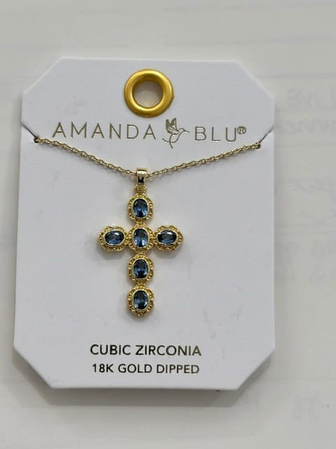 A gold cross pendant necklace with blue cubic zirconia stones, displayed on a white Amanda Blu jewelry card.