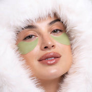 Model wearing green Patchology Cool Crush Hydrogel Eye Patches surrounded by white fur